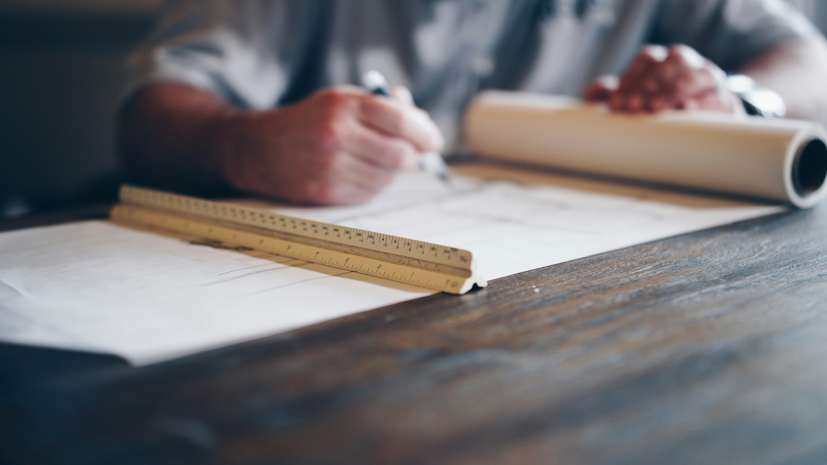An architect drafting at a desk with a scale rule